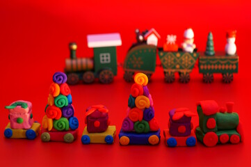 A toy Christmas train made of plasticine with gifts and Christmas trees. Bright red background. New Year decorations.