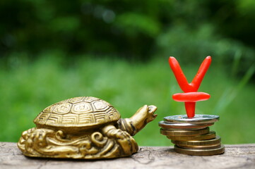 Yuan symbol and coins on a green background. There is a turtle figurine next to it. Finance and...