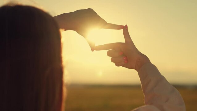 Beautiful girl shows her fingers frame symbol, sun, Sees like in movies. Hands of young female director cameraman making frame gesture at sunset in park. Seeing world as different. Business planning