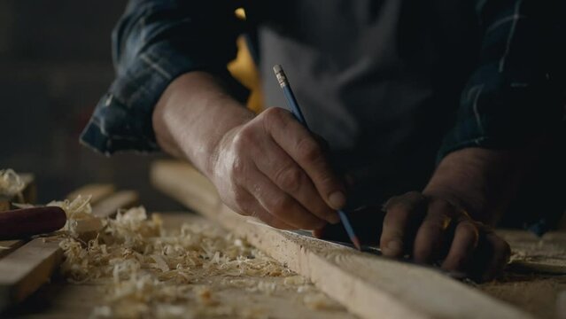 Workplace, Middle-aged builder Deeply involved Draws a mark on wood with a pencil In a furniture shop Camera in motion Novice repairman Works at a carpenter's table In a woodworking shop, fabrication