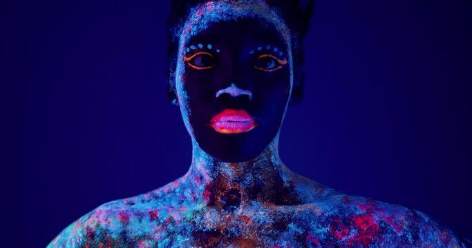 beautiful woman with sparkles on her face and body pink lips. sparking eyes looking down Girl with art make-up in color Light. Fashion model with colourful makeup Slow motion