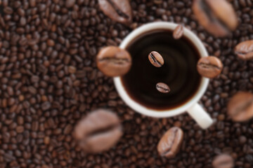 Coffee beans fall into a cup of coffee. White cup with coffee on the background of coffee beans. Energy drink, caffeine. Selective focus