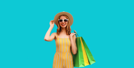 Happy smiling young woman posing with shopping bags wearing summer straw hat on blue background