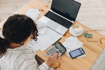 Top view of a woman working at home in the kitchen with financial papers, counting on a calculator, paying bills, planning a budget to save some money. Independent accounting, remote accountant - obrazy, fototapety, plakaty