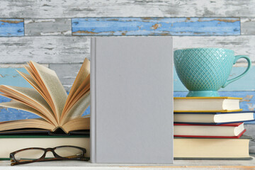 Book cover mock up - plain book against stacks of books with mug & glasses.