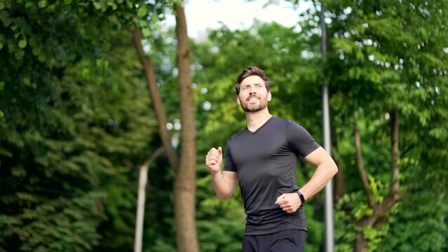 Handsome bearded male runner running on a urban park Sporty atlet man jogger jogging outdoors look at result a fitness tracker bracelet or smartwatch Active male enjoys morning activities in fresh air