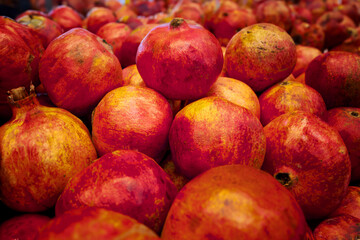 A large pile of pomegranates on the fruit market counter. Close-up of ripe red pomegranates with spots on market counter for sale.