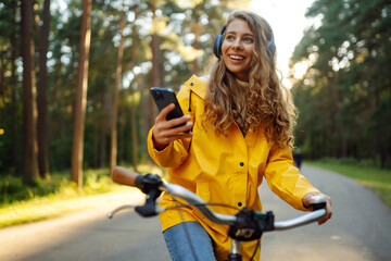 Beautiful woman with headphones and smartphone rides a bicycle listening to music. Active lifestyle, vacation, resting. Communication in social networks. Lifestyle.