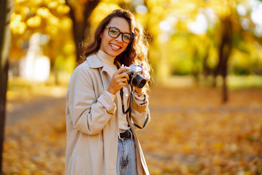 Beautiful woman taking pictures in the autumn forest. Smiling woman enjoying autumn weather. Rest, relaxation, tourism, lifestyle concept.