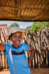 young village african woman with a hat standing under the shad of a shack