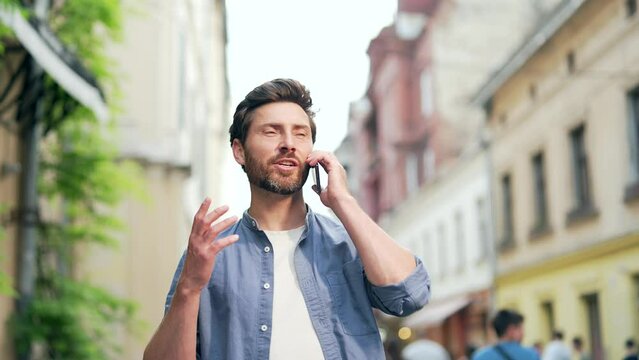 Happy adult man in casual clothes is talking on a mobile cell phone while standing on a city street. A tourist traveling on a trip communicates with relatives via roaming communication in the old town