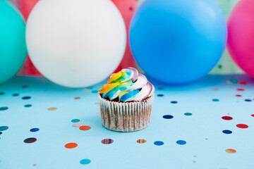 One rainbow color cupcake on blue background with colorful air balloons	