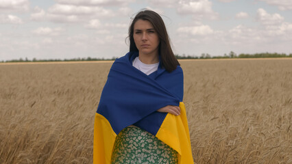 Portrait of Ukrainian patriotic woman stands in wheat field with blue-yellow flag of Ukraine