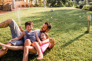 Single father playing with his two kids in the backyard with a water hose