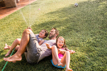 Father playing with his kids in the backyard with a water hose