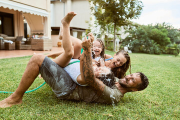 Young family playing in the backyard with a water hose