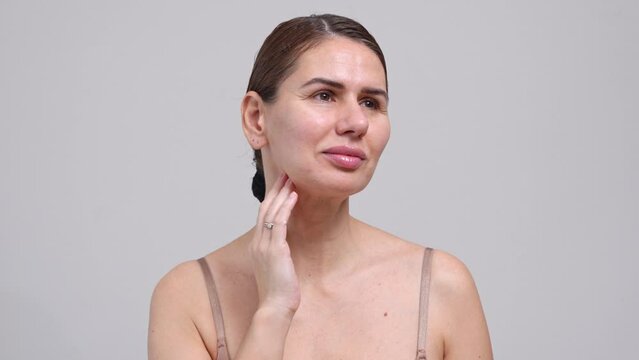 Middle Aged Woman Touching Face Skin White Background. Female 40 Year Lady Looking At Camera Smiling. Concept of Enjoying Her natural beauty, High Self Esteem, Wellness. Natural Cosmetic Skincare