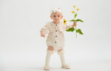 small baby in full growth on a white background.girl 14 months old in light clothes on a white background with a yellow flower isolated