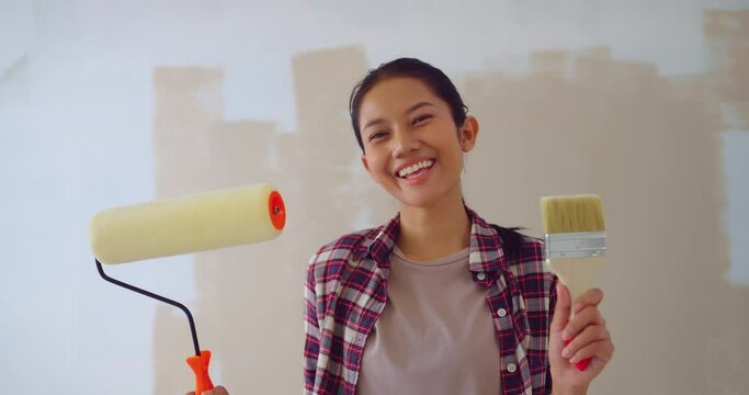 Portrait of Attractive Young woman holding roller in hand prepare to paint wall in apartment. Young woman looking to camera with smiling at wall in apartment.