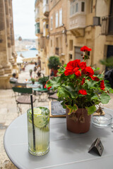 Fototapeta na wymiar Drinking mojito in a cafe on a Triq San Gwann street, with a view to the Grand harbour of Valletta, Malta. Mediterranean Sea.