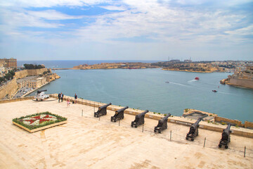 Cannons and Maltese cross in the Upper Barrakka Gardens, Valletta, Malta. View over the Grand Harbour and the Three Cities, Mediterranean sea. 