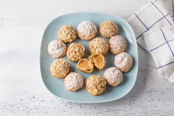 Gluten-free oat profiteroles with caramel cream of boiled condensed milk, sprinkled with powdered sugar and nuts on a light blue background, top view. Delicious healthy homemade food