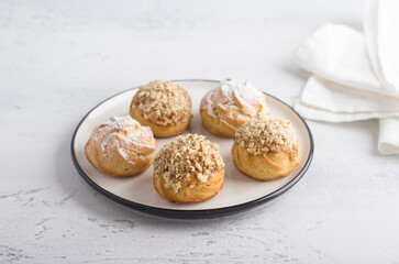 Gluten-free oat profiteroles with caramel cream of boiled condensed milk, sprinkled with powdered sugar and nuts on a light blue background, top view. Delicious healthy homemade food