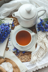 Cup of tea, open book and cornflowers, top view