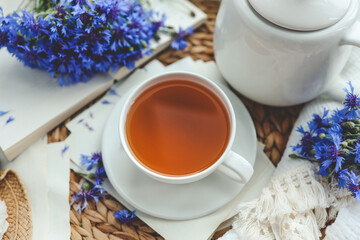 Cup of tea, open book and cornflowers, top view