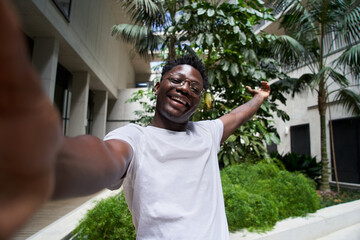 Selfie of a young black man standing outside and laughing with a hand up. African people. Cheerful...