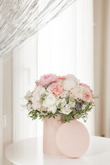 An elegant bouquet of fresh roses, peonies, and daisies in a pink box, beautifully arranged and placed by a light-filled window.