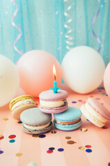 Macarons and one candle on blue and pink background with air balloons, vertical card with copy space