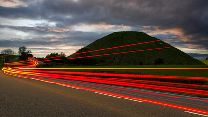 Vehicle light trails past Silbury Hill ancient monument in Wiltshire, England.