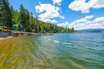 View from the public beach of waterfront homes, marina and the mountains surrounding Carlin Bay, one of the bays on Lake Coeur d'Alene, in Coeur d'Alene, Idaho, in the North Idaho Panhandle. - obrazy, fototapety, plakaty