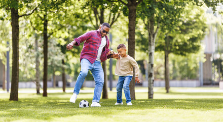 Happy ethnic family father and son playing football in the park in summer