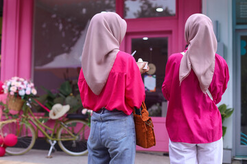 Rear view of two unidentified woman wearing hijab in front of cute pink cafe. All about pink