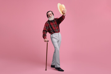 Senior man with hat and walking cane on pink background