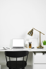 Cozy workspace with laptop, lamp and stationery on wooden desk at home