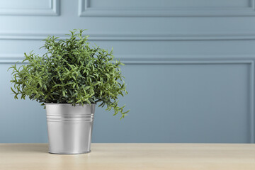 Beautiful artificial plant in flower pot on wooden table near grey wall, space for text