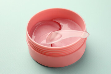 Jar of under eye patches with spoon on turquoise background, closeup. Cosmetic product
