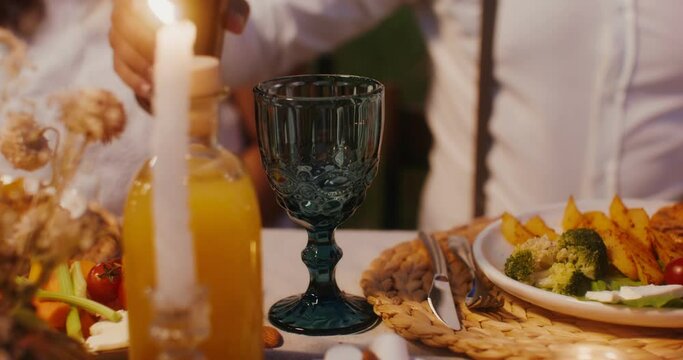 A man pours wine into a glass sitting at a beautifully served festive table, close-up of hands, no face
