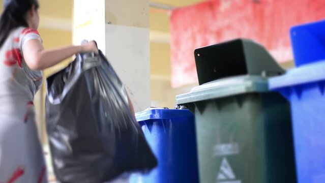 A woman is  throwing trash into a garbage bin