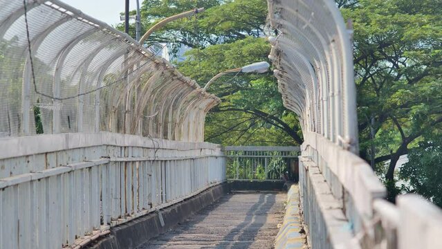 A quaint, rusty and deserted urban pedestrian bridge with a large tree in the background. Depicts the loneliness, neglect, and abandoned side of the city. Shot with a telephoto lens and handheld.