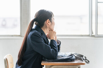 学校の教室で女子高校生・中学生が俯いて悩んでいる（悩む・困る・ストレス）
