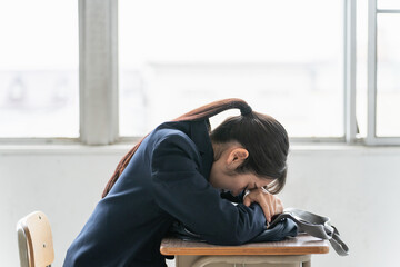 学校の教室で女子高校生・中学生が俯いて悩んでいる（悩む・困る・ストレス）
