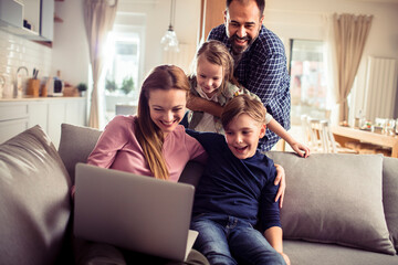 Young family spending time together at home and using a laptop on the couch