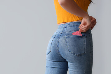 Young woman with condom in pocket on light background, back view - obrazy, fototapety, plakaty