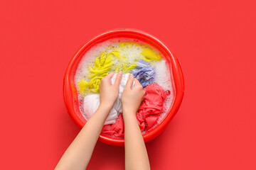Woman washing laundry in plastic basin with water and foam on red background - obrazy, fototapety, plakaty