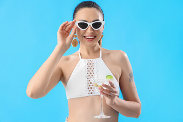 Beautiful woman in swimsuit with martini on blue background