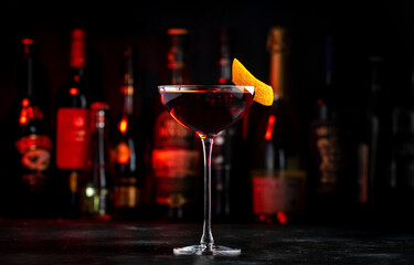 Fototapeta na wymiar Adonis alcoholic cocktail drink with sherry and red vermouth, black bar counter background, steel tools and bottles